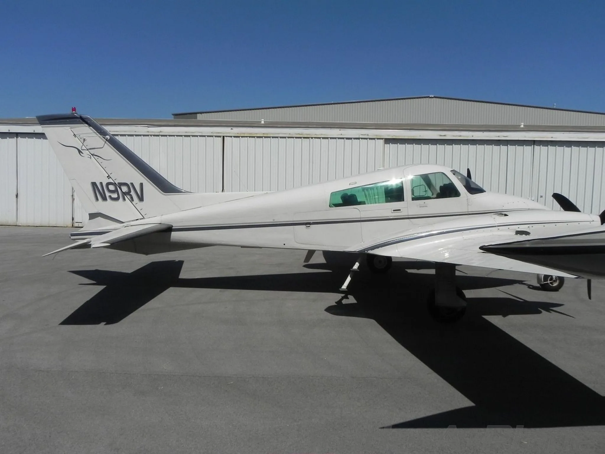 A side profile of a white twin-engine Cessna 310 aircraft showing the tail number N9RV and a stylized logo on the vertical stabilizer.
