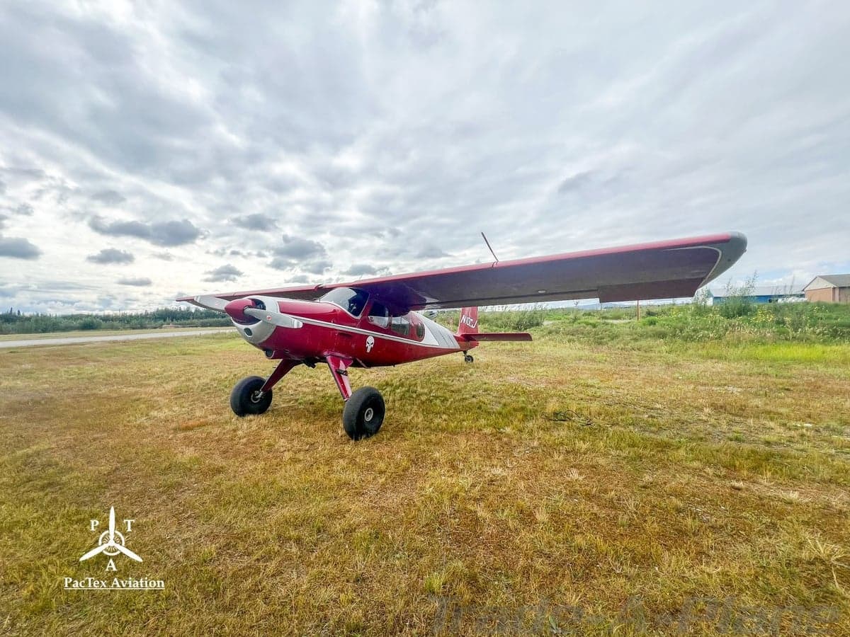 A red and silver single-engine aircraft with large tires, registration N10CJ, viewed from the front-left on a grassy field.
