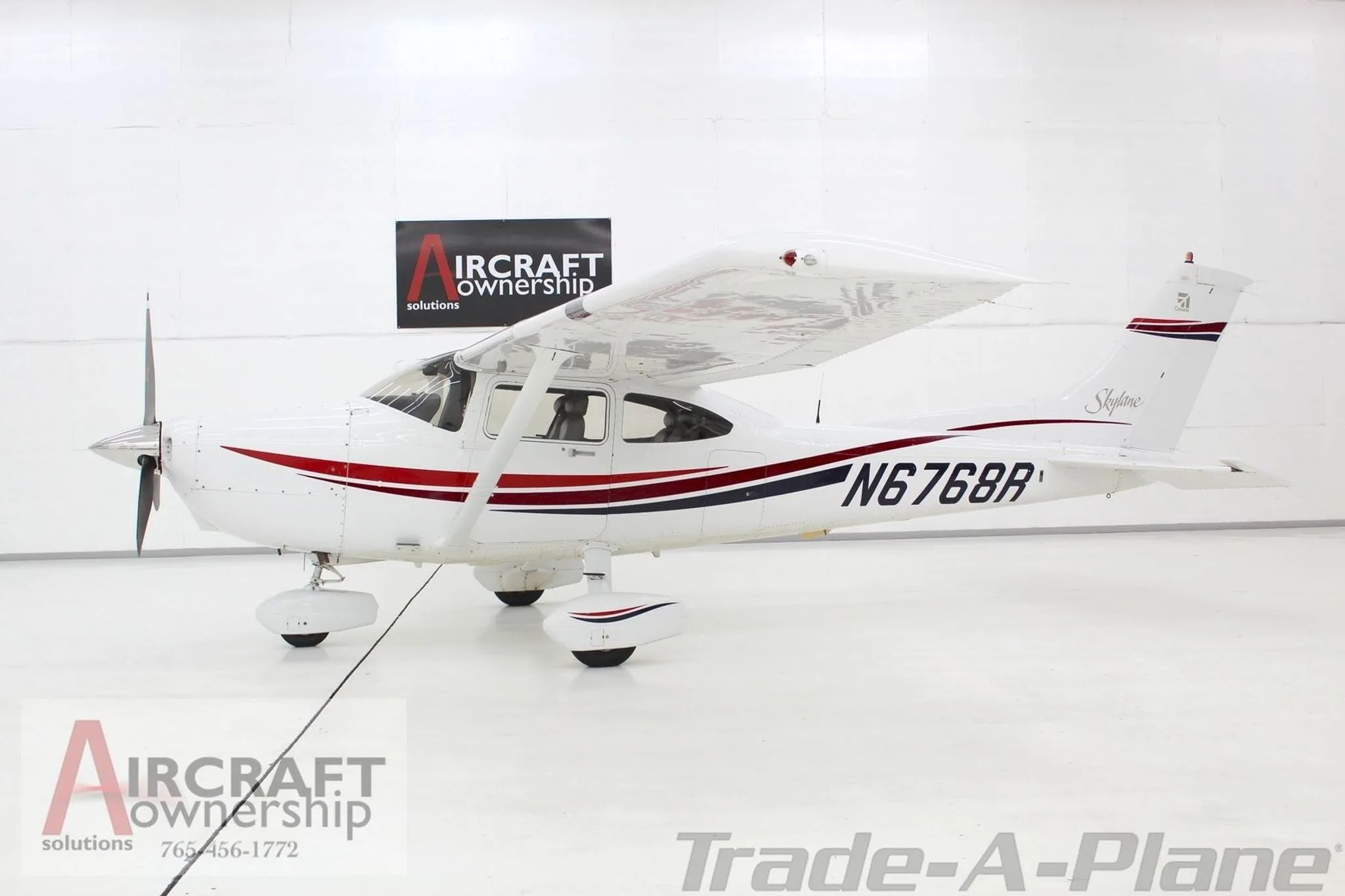 A white Cessna Skylane N6768R with red and blue stripes is parked in a hangar.