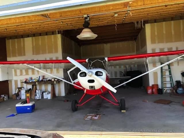 A red and white light aircraft, possibly a biplane, viewed from the front inside a hangar.