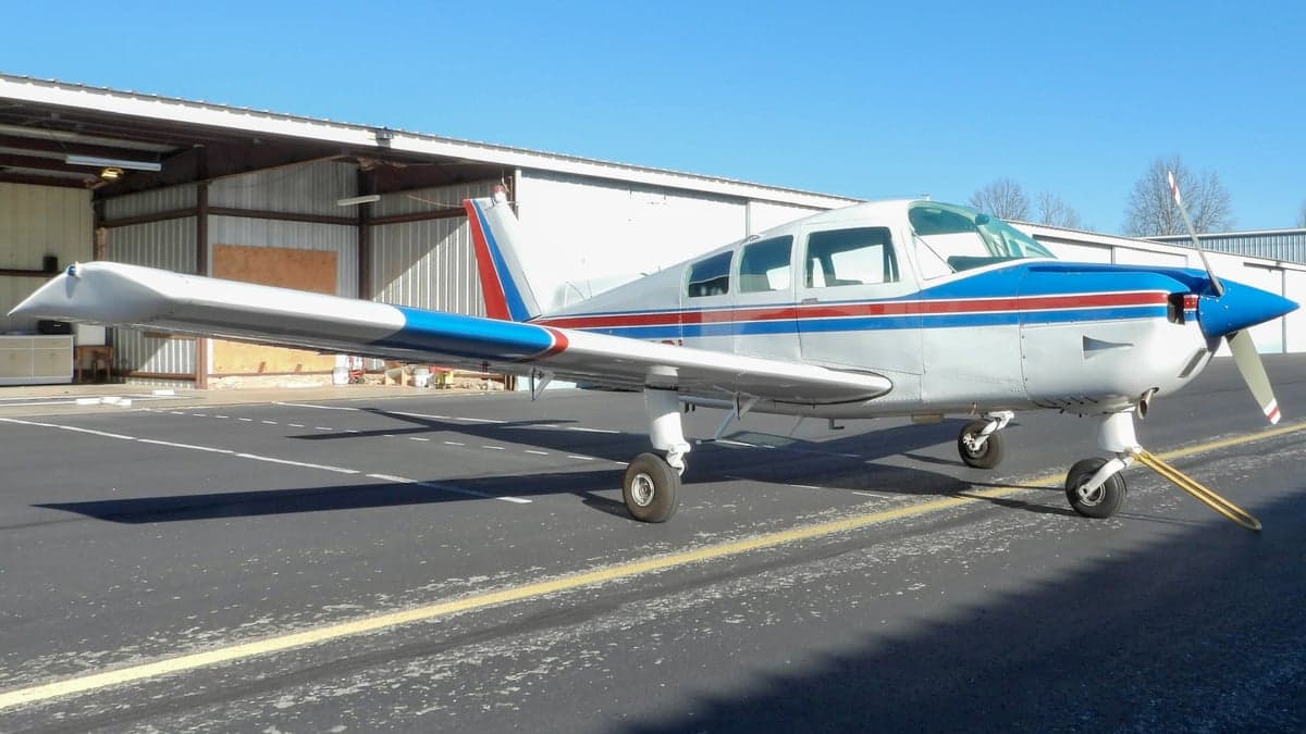 Three-quarter view of a Piper PA-28-140 Cherokee with blue nose and red tail.