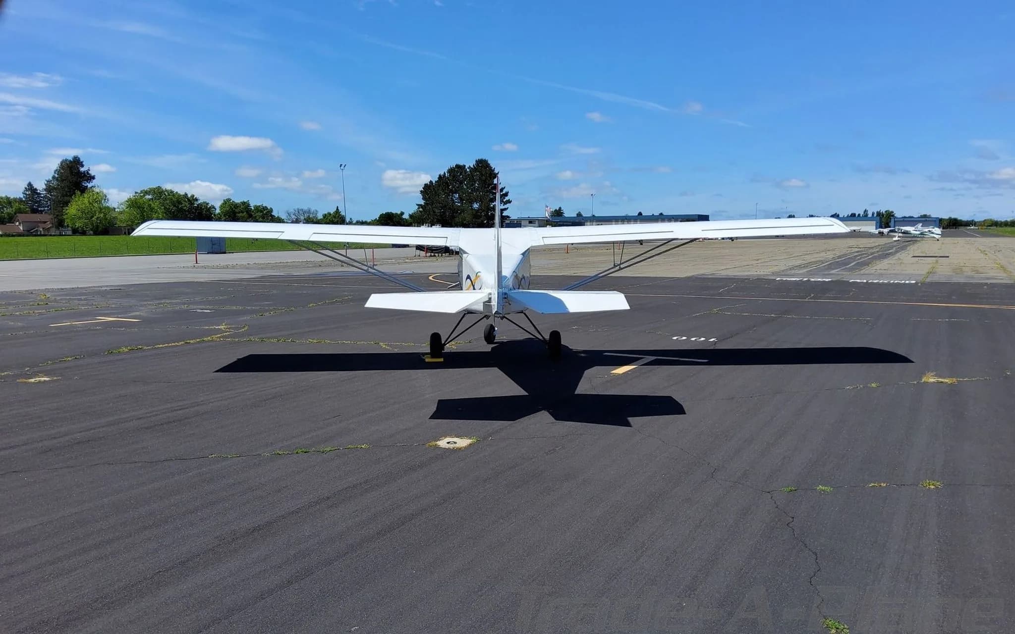 A white BushCaddy aircraft viewed from the rear, parked on a sunny tarmac.