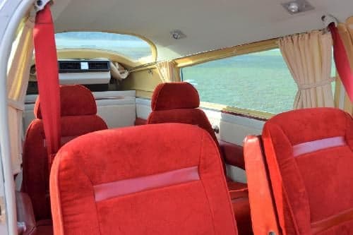 Interior view of the aircraft cabin with red seats and cream-colored curtains.