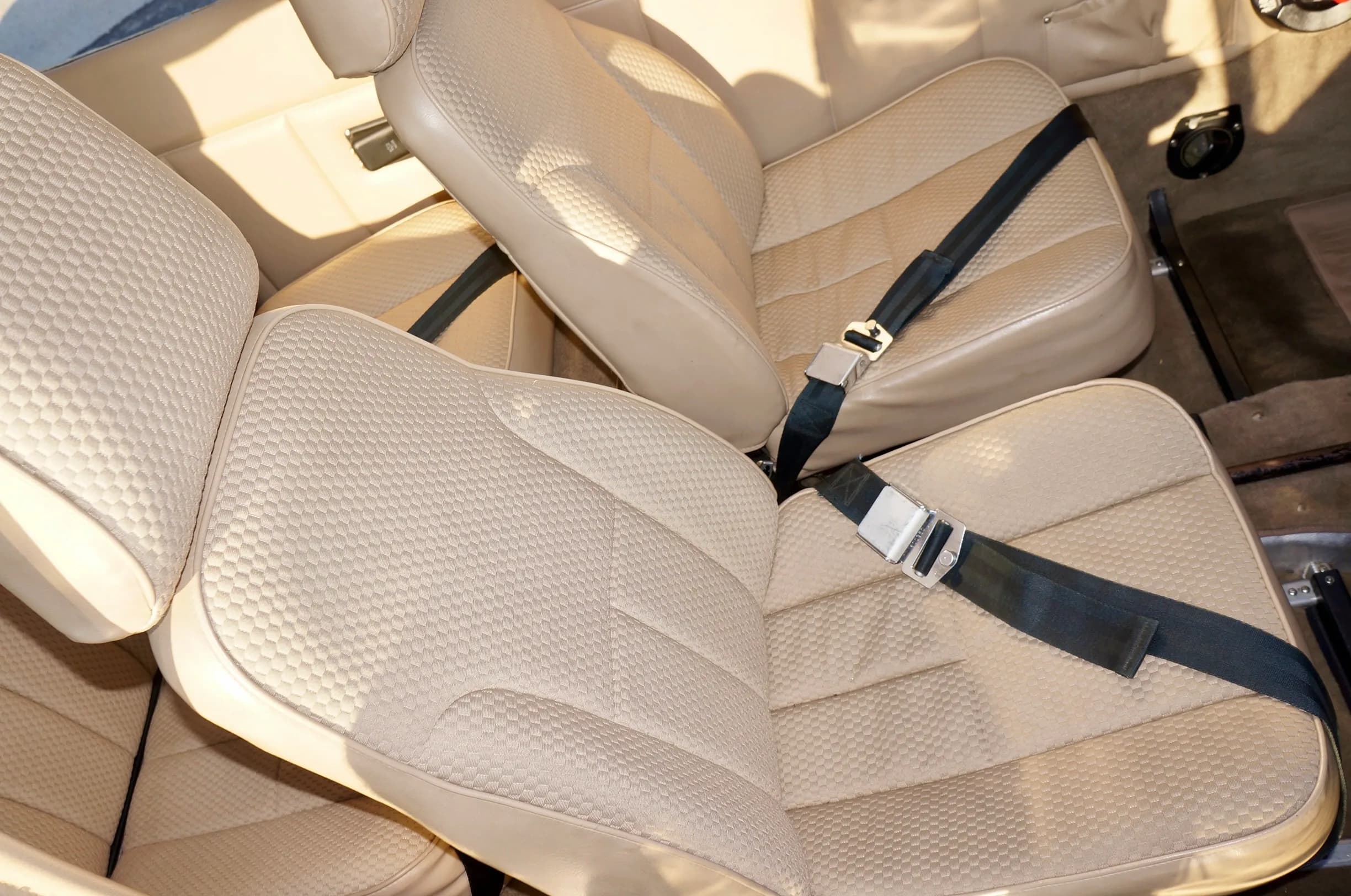Close-up view of the textured beige front seats with black seatbelts in the aircraft cabin.