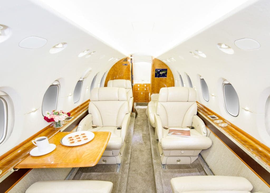 Interior of the aircraft with beige leather seats, wood accents, and a table with a tablet and coffee cup.