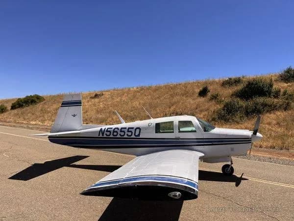 A white single-engine propeller aircraft with blue stripes (N5655Q) is parked on an asphalt surface under a clear blue sky.