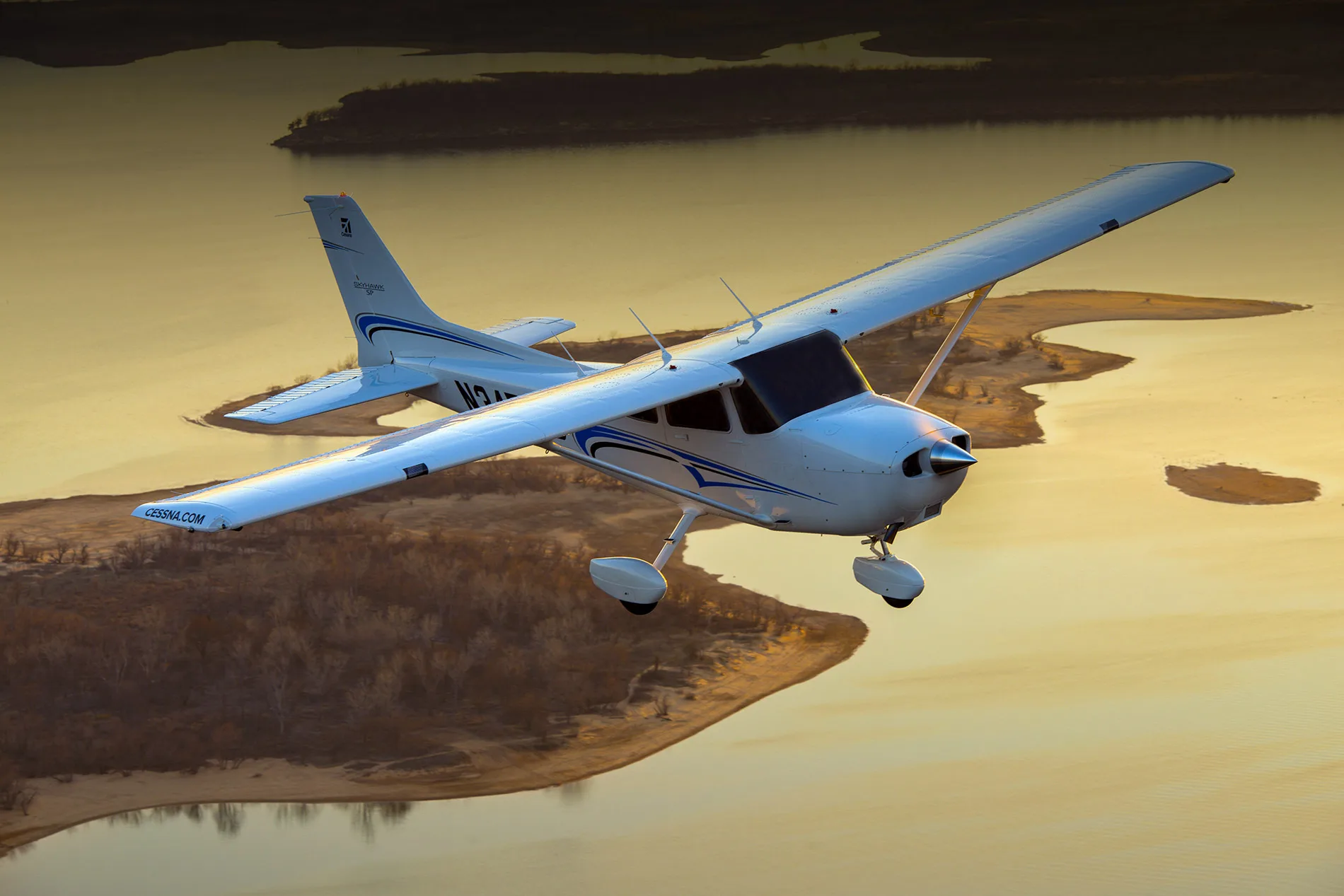 A Cessna 172 Skyhawk in flight over a lake at sunset.