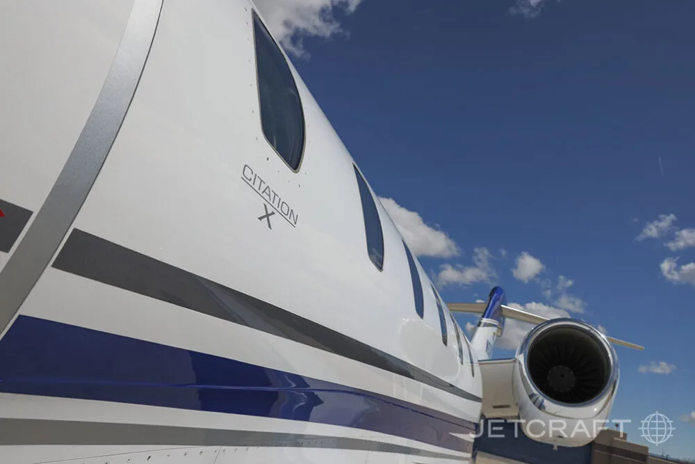 A close-up view of the fuselage and engine of a white and blue Cessna Citation X, showing the 'CITATION X' text.