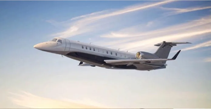 A sleek silver and dark grey business jet flying through a partly cloudy sky.