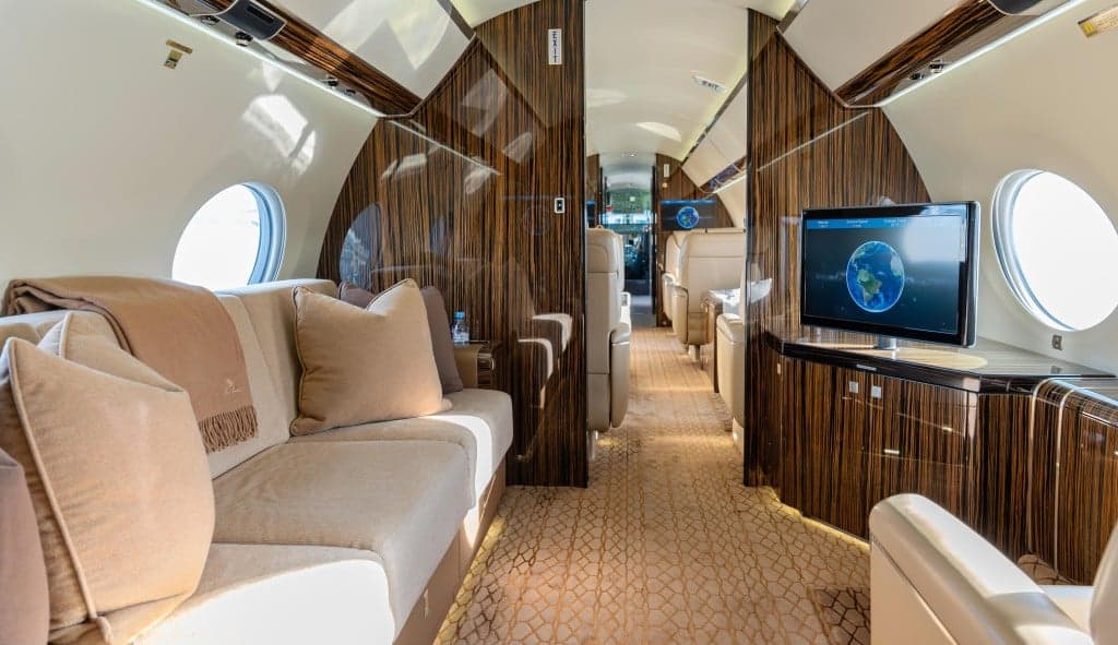 The interior of the aircraft with beige leather seats, wood paneling, and a dining table set for a meal.