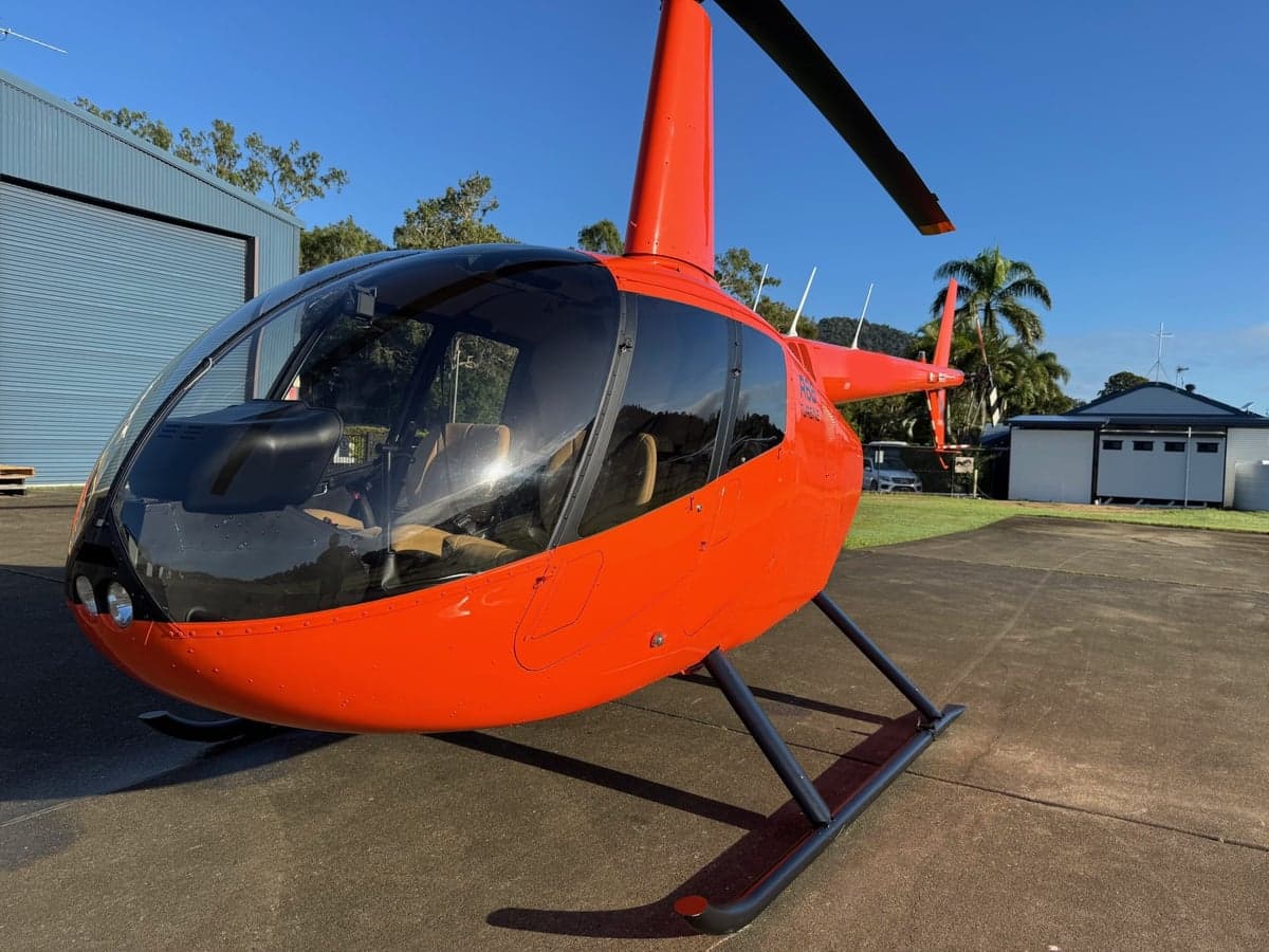 An orange Robinson helicopter parked on the tarmac.