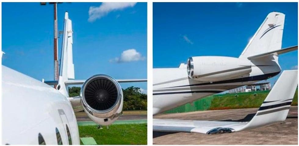 A close-up of the tail and engine of a white jet aircraft with black stripes on the tarmac.