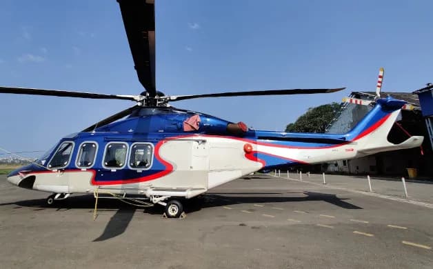 A blue, white, and red helicopter with a unique paint scheme parked on an tarmac under a clear sky.
