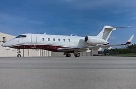 A white and maroon private jet parked on a runway in front of a building.
