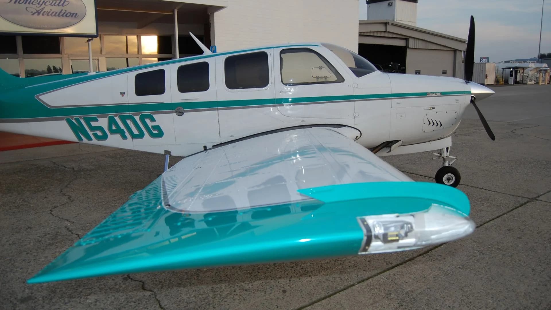 A close-up of the wing and fuselage of the Beechcraft Bonanza N54DG, showing the teal and white paint scheme.