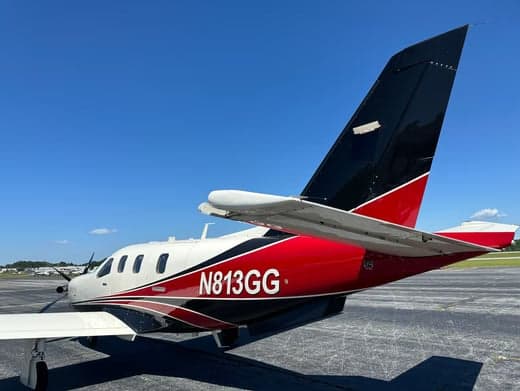 A rear-side view of a white, red, and black single-engine turboprop aircraft (N813GG) parked on an airfield.