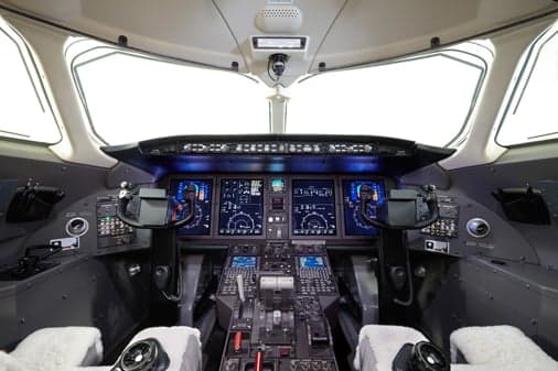 The modern glass cockpit of a business jet with multiple digital displays and control yokes.