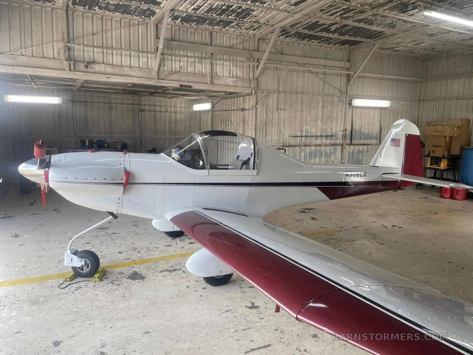 A side view of a white and maroon experimental aircraft with tail number N306CX, parked in a hangar.