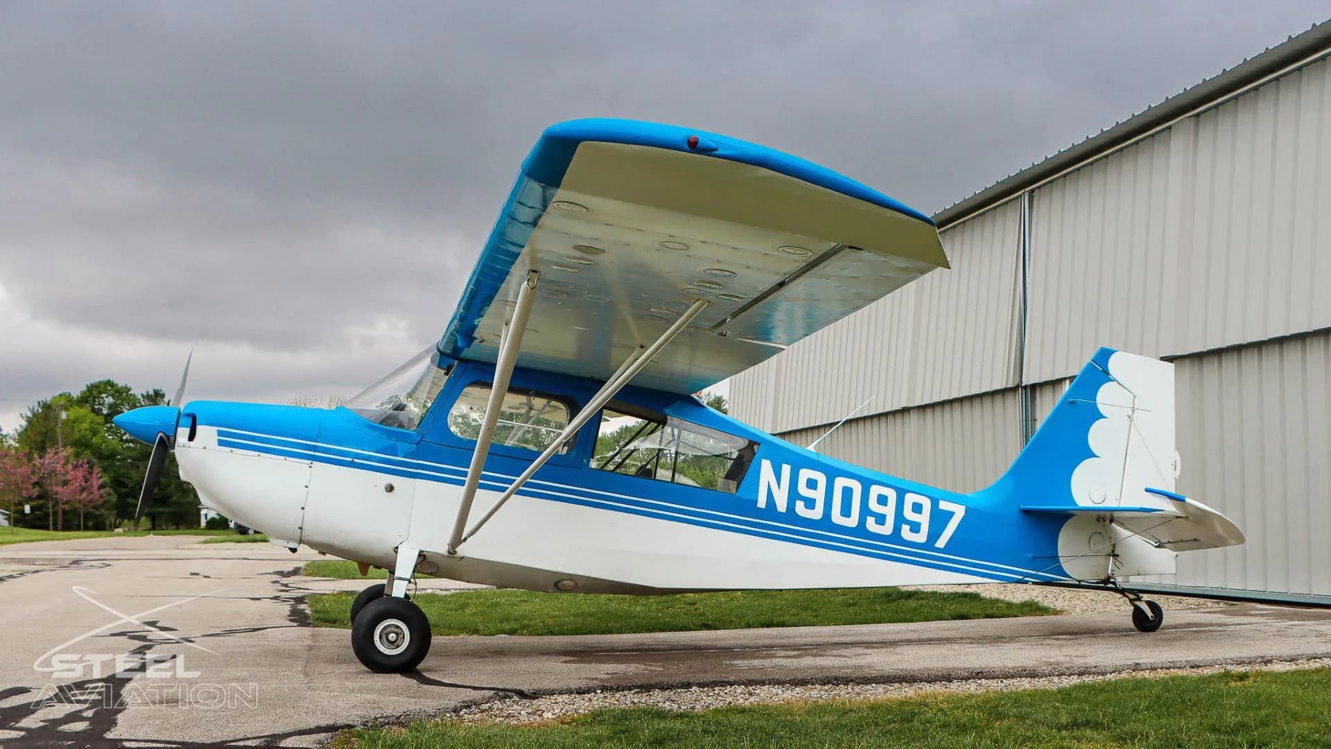 Side profile of a white and blue Bellanca 7GCBC Citabria aircraft with registration N90997, parked on an asphalt ramp.