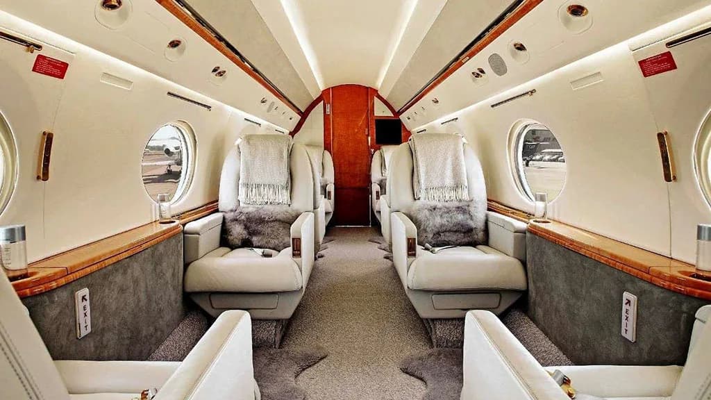 The luxurious interior cabin of a private jet with light-colored individual seats and wood paneling.