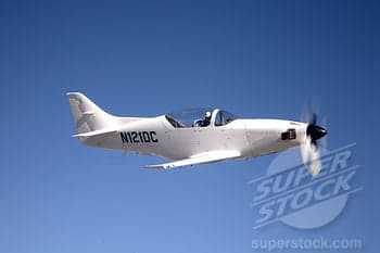 A white aircraft with tail number N121DC is in flight against a blue sky.