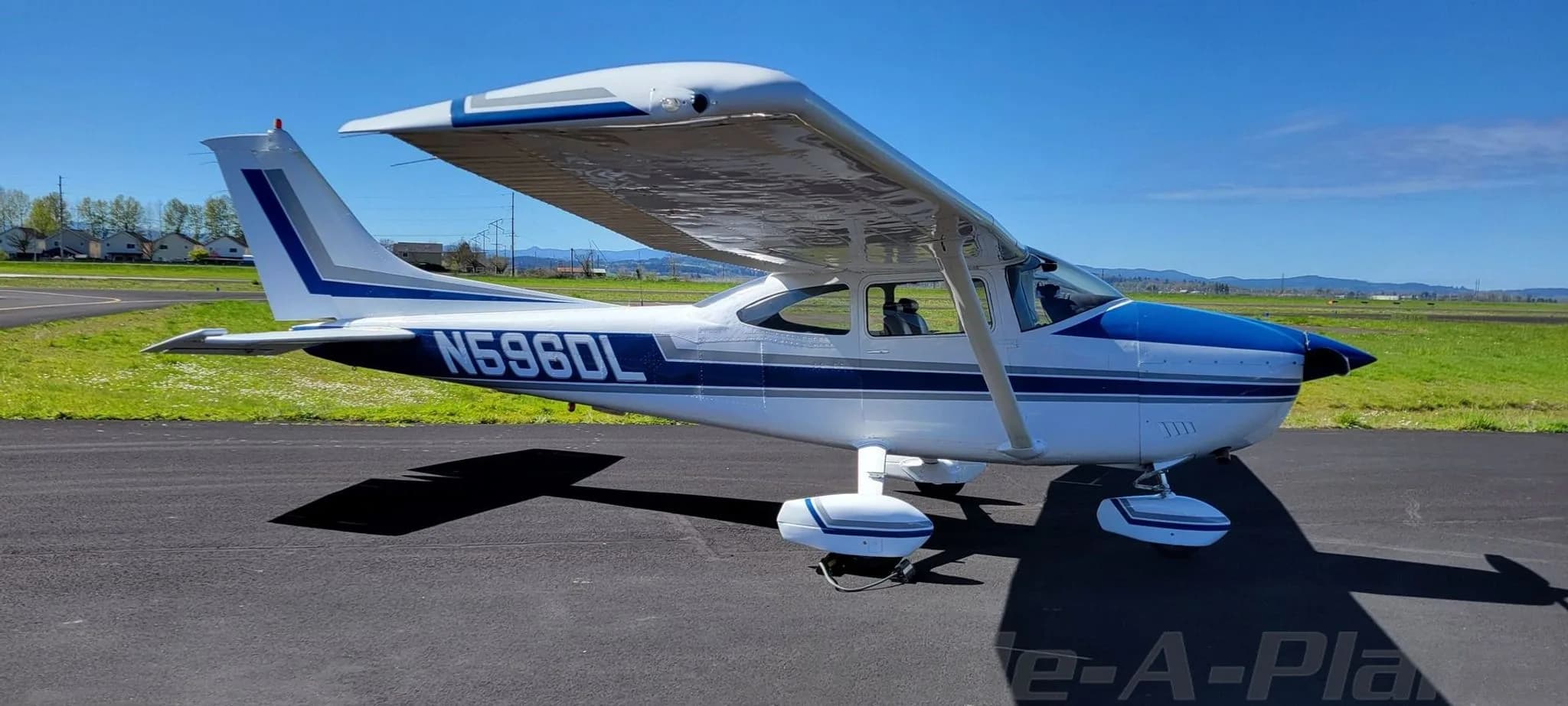 Side view of a white and blue Cessna 182 Skylane aircraft with registration N596DL on an airfield.