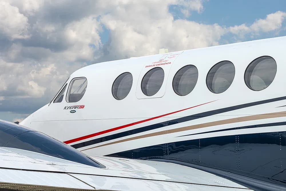 A close-up view of the front fuselage of a white King Air 350 aircraft with black, red, and gold stripes, showing the cockpit and passenger windows.