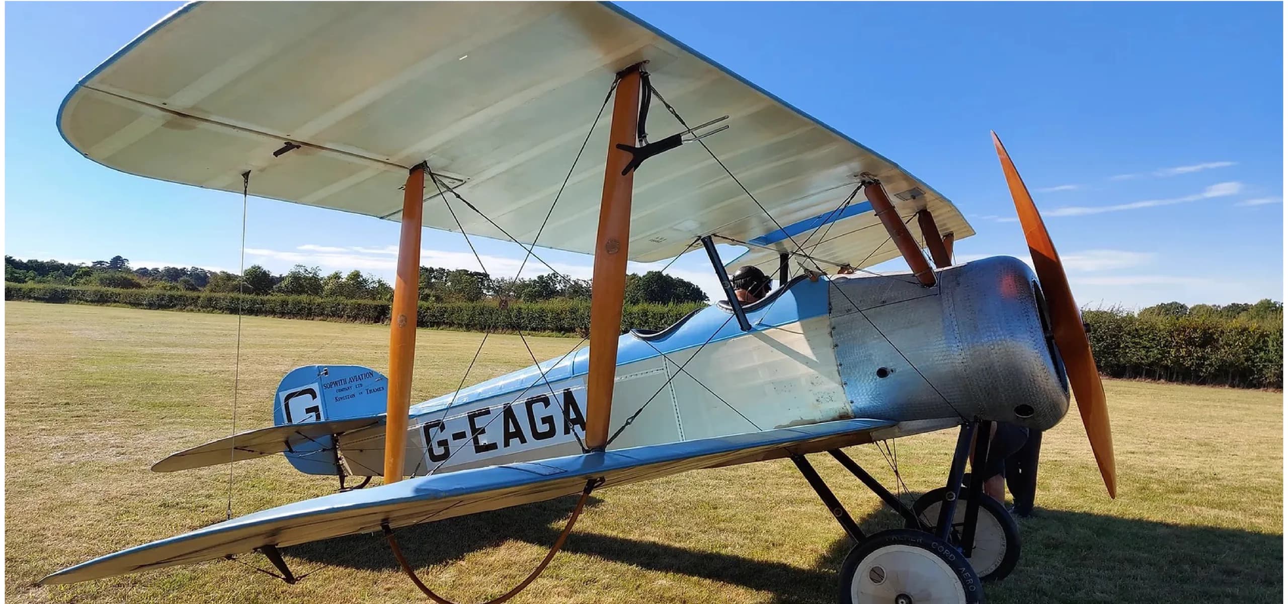 A vintage biplane with registration G-EAGA is parked on a grassy field.