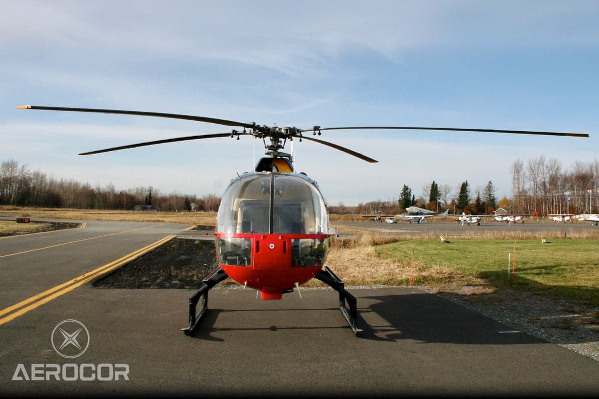 Front view of a red and black MBB BO-105 helicopter parked on an airfield.