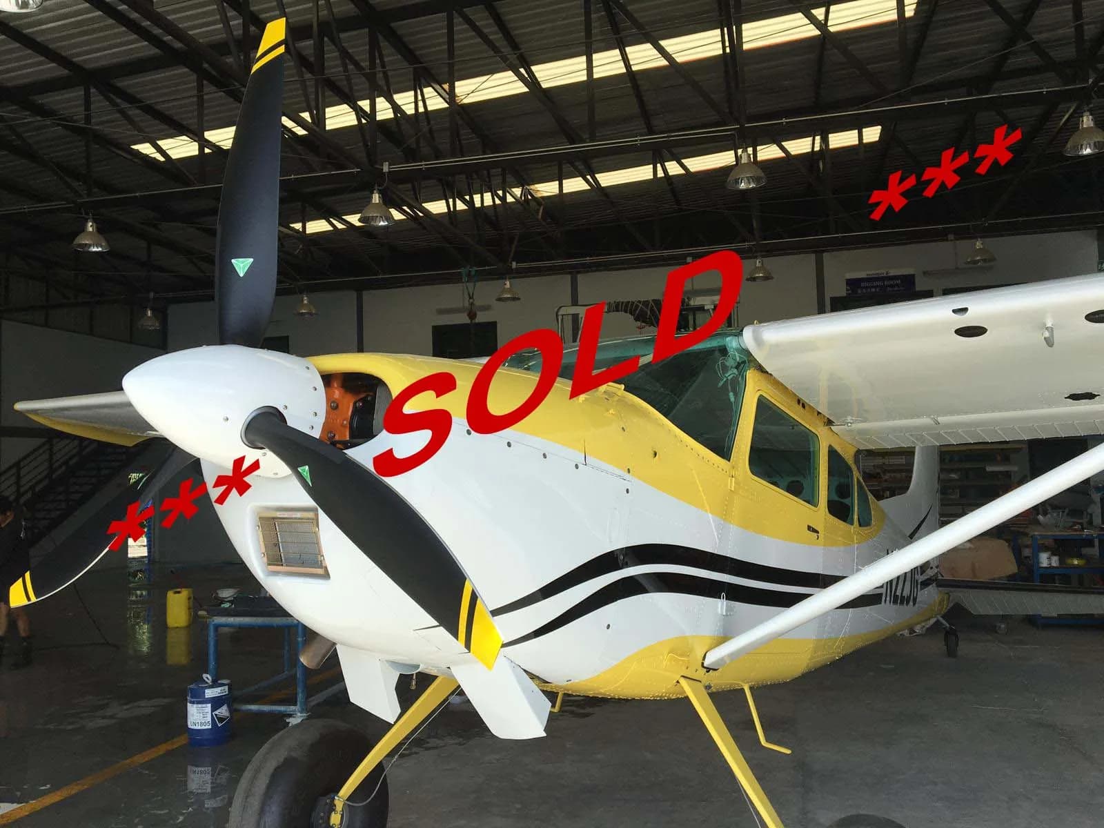 A yellow and white single-engine propeller aircraft with black stripes is parked in a hangar, with 'SOLD' text overlaid.