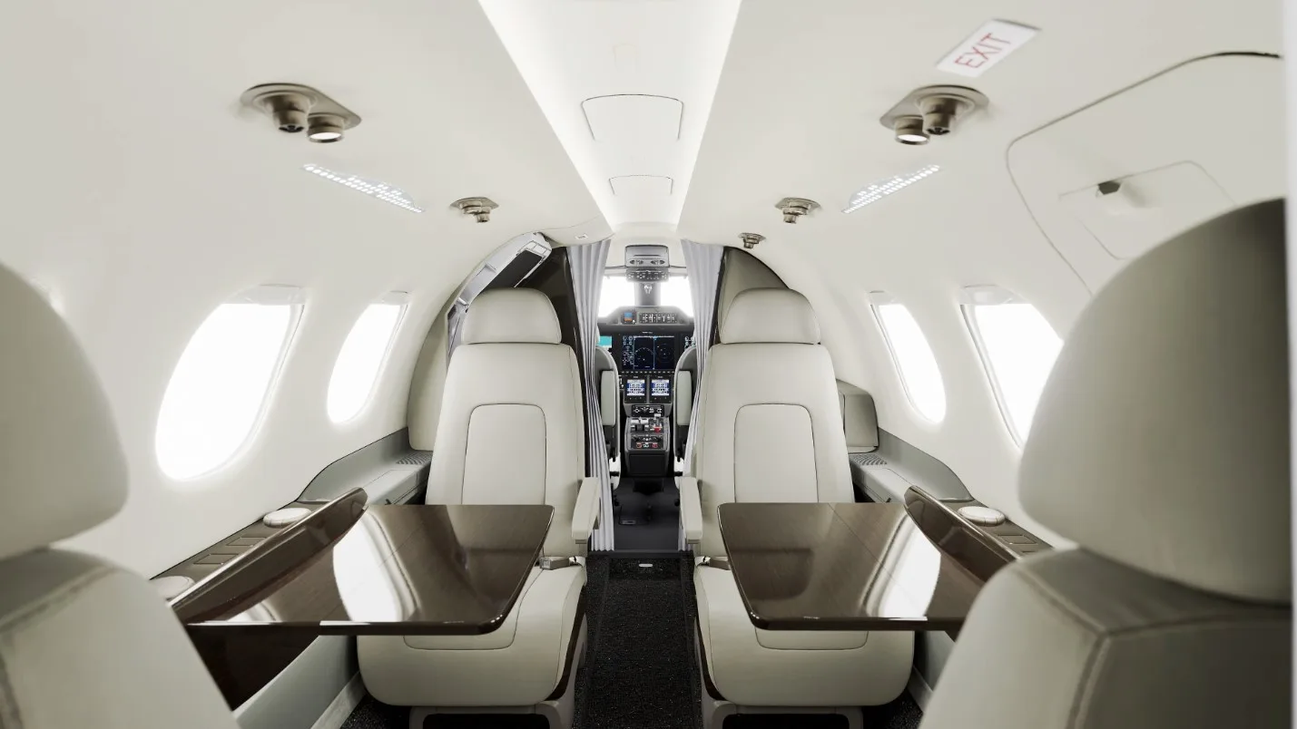 View of a business jet's cabin interior, looking forward towards the cockpit, with light seats and dark tables.