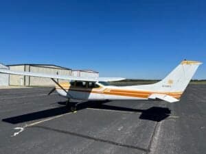 A Cessna 182RG on the tarmac with a white and gold paint scheme, showing the tail number.
