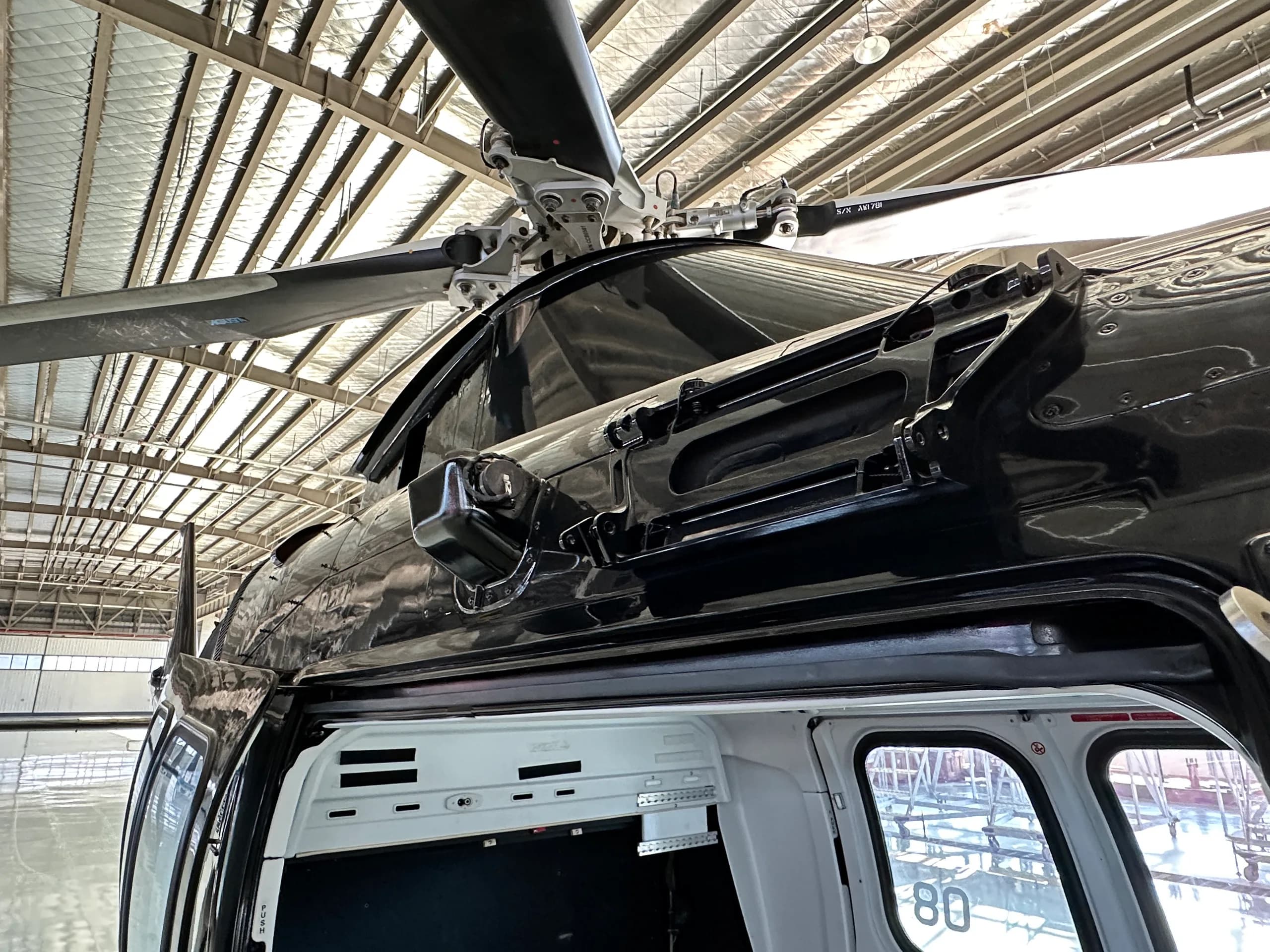 A close-up view of the black helicopter's rotor mast and upper fuselage, with an open door revealing the interior.