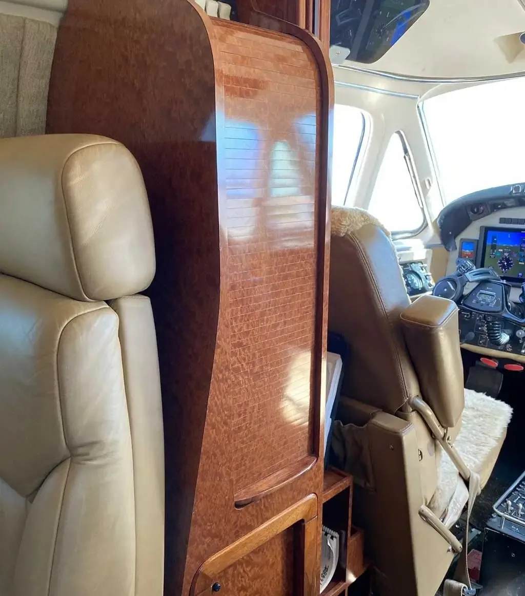 View from the aircraft cabin showing a wooden cabinet and tan leather seats, with the cockpit partially visible in the background.