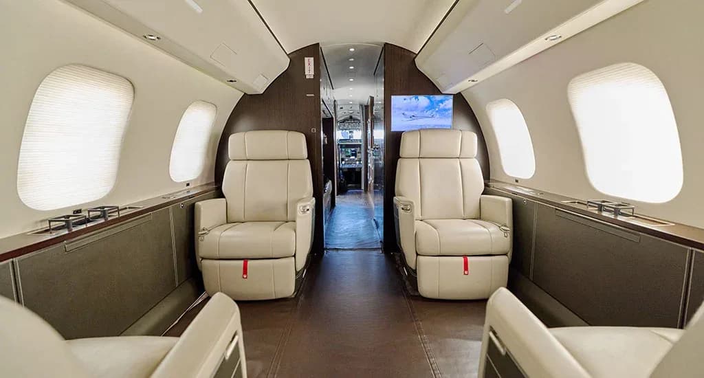 The forward cabin of a private jet with cream leather seats and a screen displaying an aircraft image.