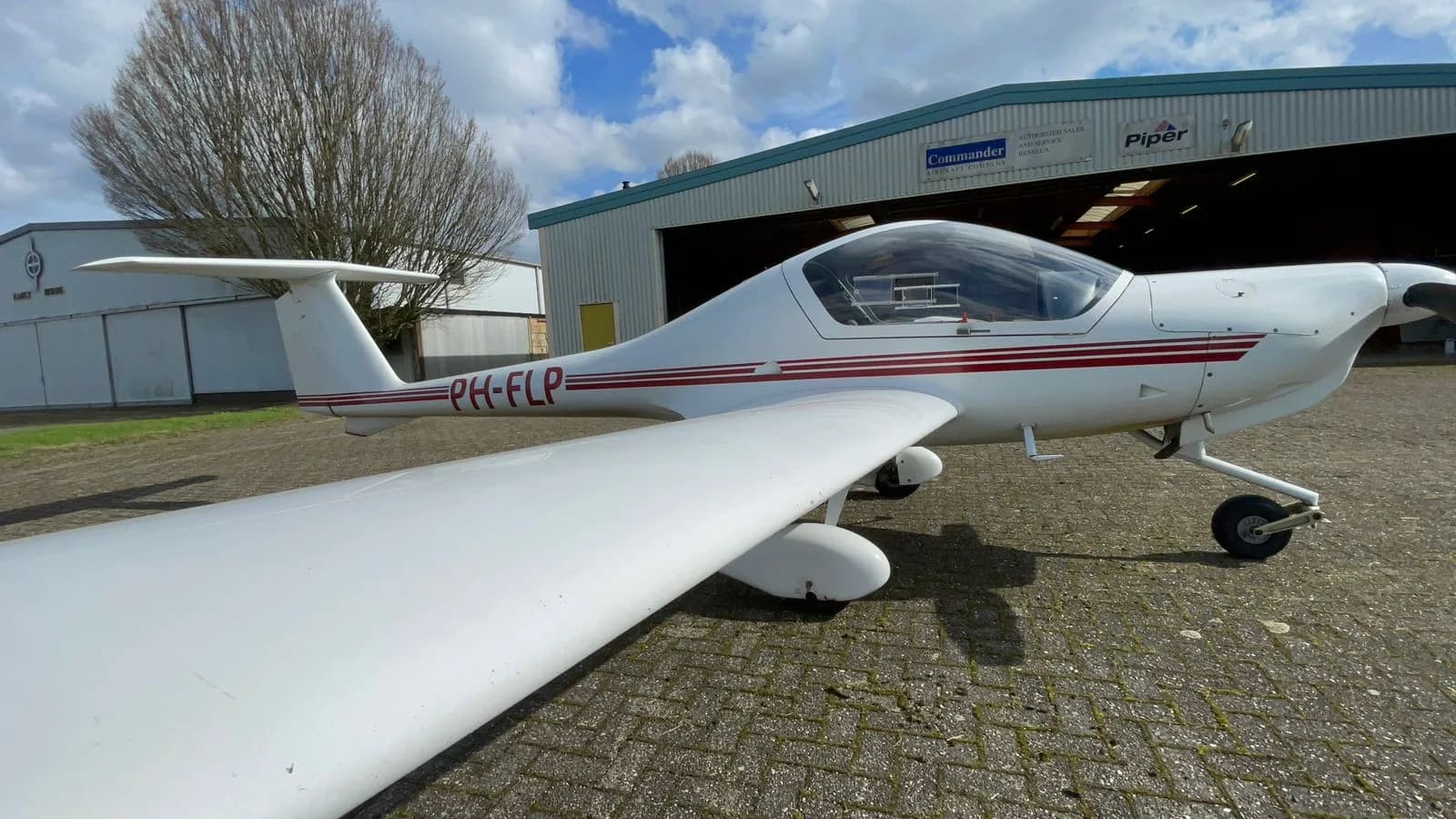 Diamond DV20 Katana aircraft with registration PH-FLP parked near a hangar.