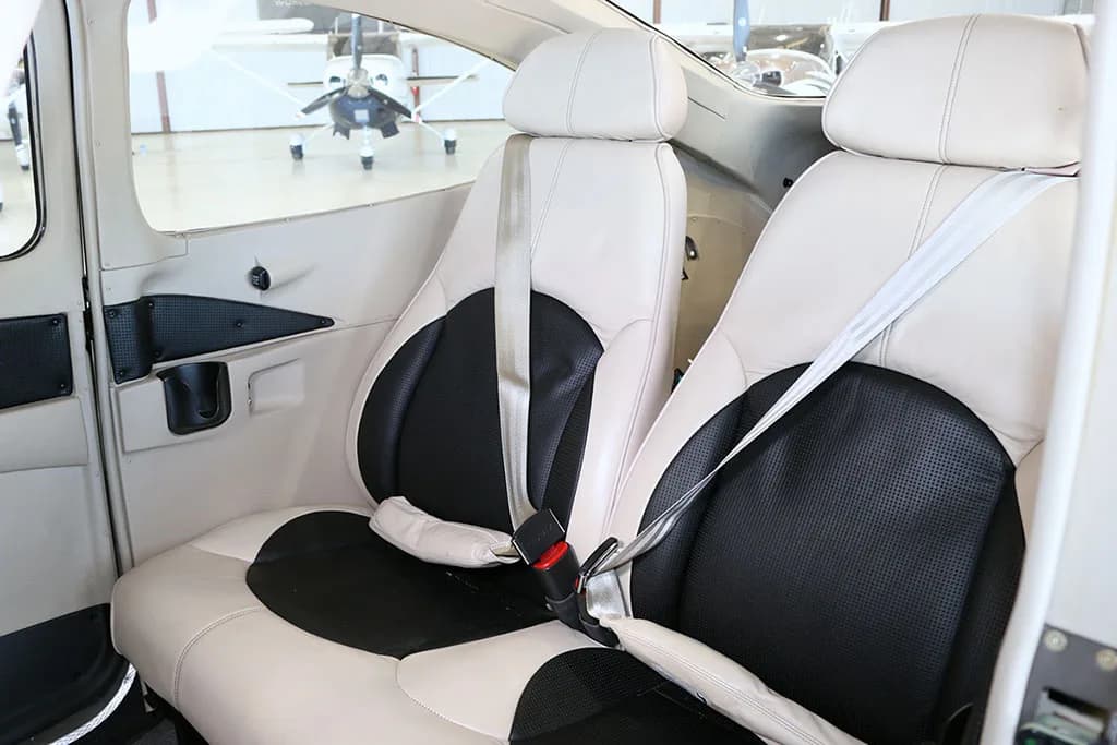 The light-colored leather and black fabric passenger seats with seatbelts are visible inside the aircraft cabin.
