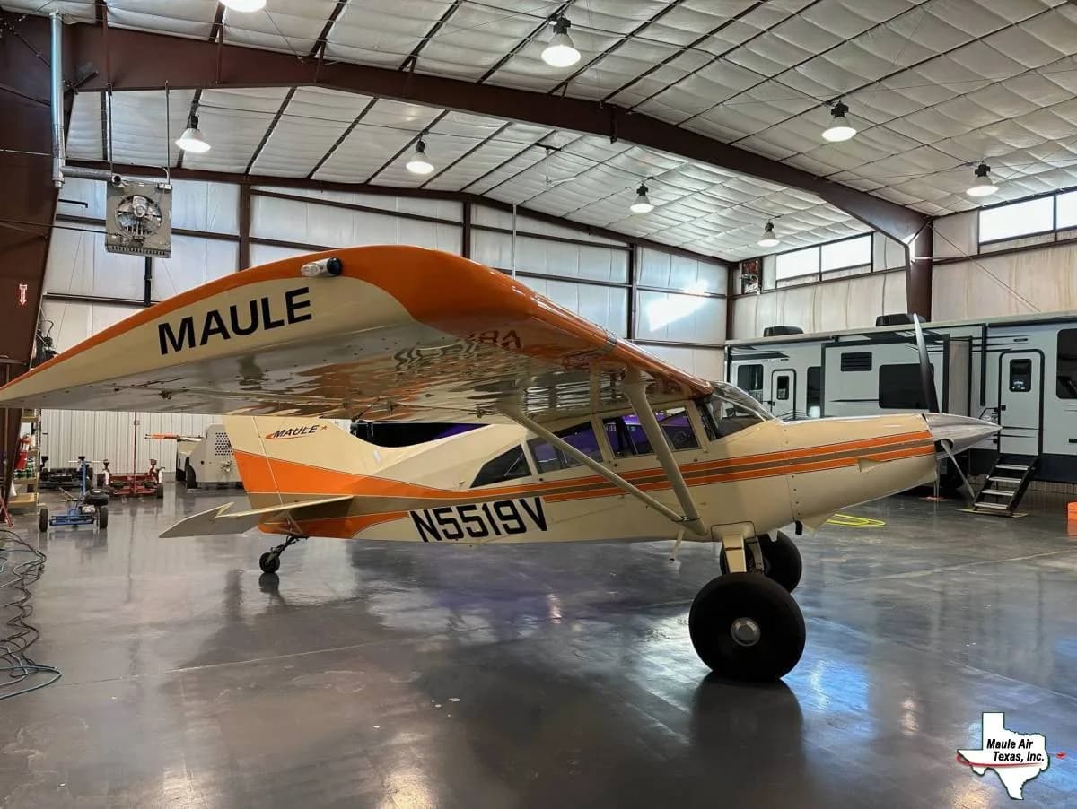 A Maule aircraft with registration N5519V, painted white and orange, parked inside a hangar.