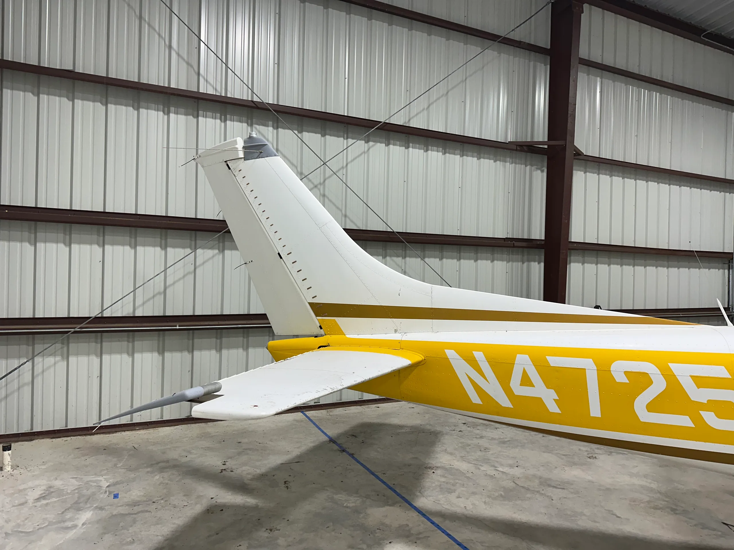A close-up view of the tail section of the yellow and white Cessna 172, N4725K, in a hangar.