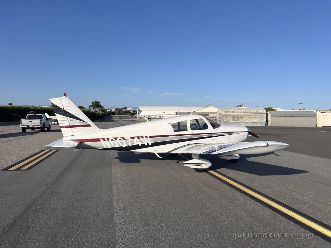 A white single-engine propeller aircraft with red and black stripes, parked on an asphalt runway or taxiway.