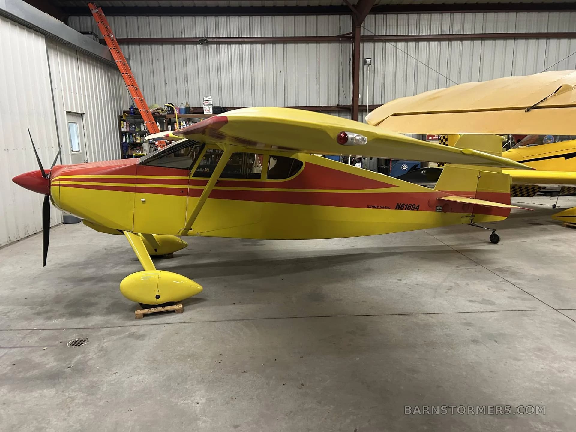A yellow and red single-engine aircraft with tail number N61694 is parked in a hangar, viewed from the side.