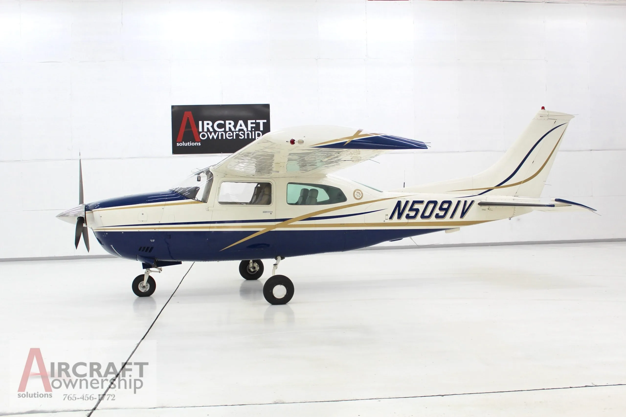 A blue and white Cessna 206 aircraft, N5091V, parked in a brightly lit hangar.