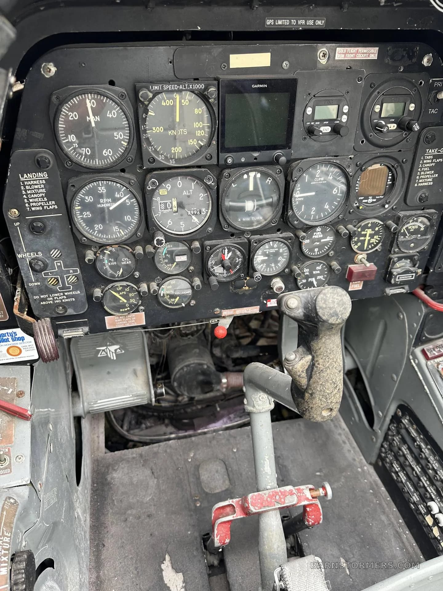 A close-up view of the instrument panel and control stick in a vintage aircraft cockpit, showing various gauges and switches.