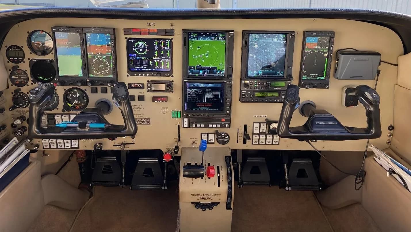 The cockpit of a Piper Malibu Mirage, featuring a modern glass panel avionics suite with multiple displays and traditional yokes.
