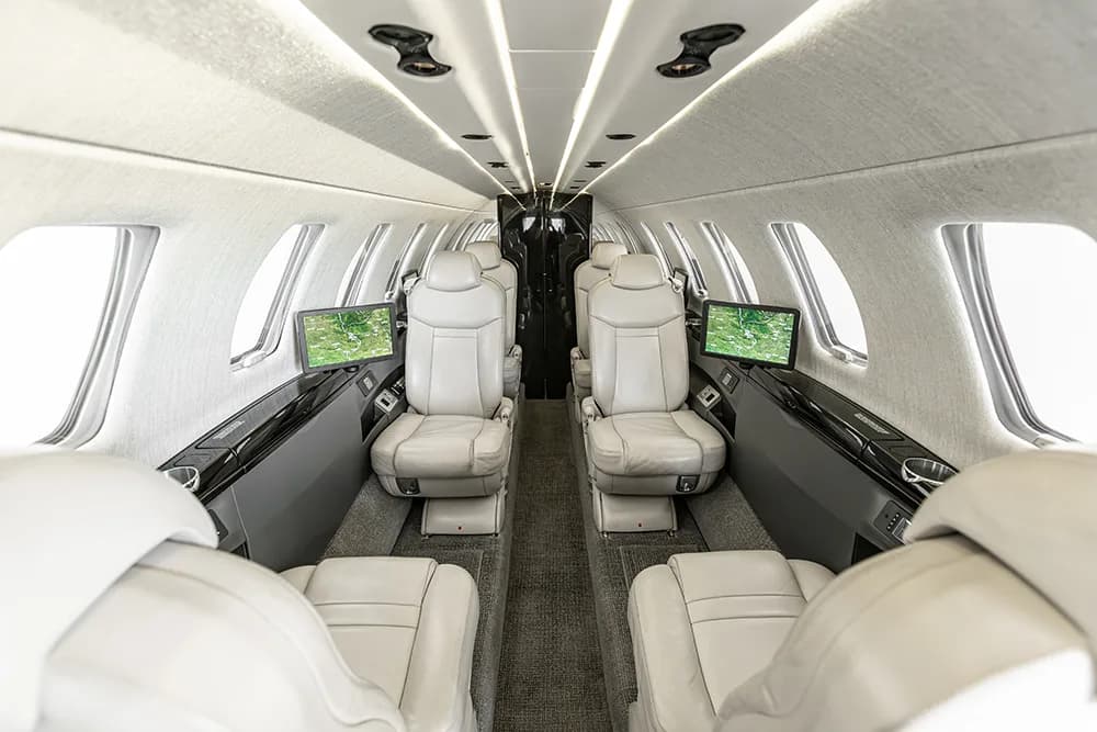 A view of the luxurious private jet cabin with light grey leather seats and individual entertainment screens.