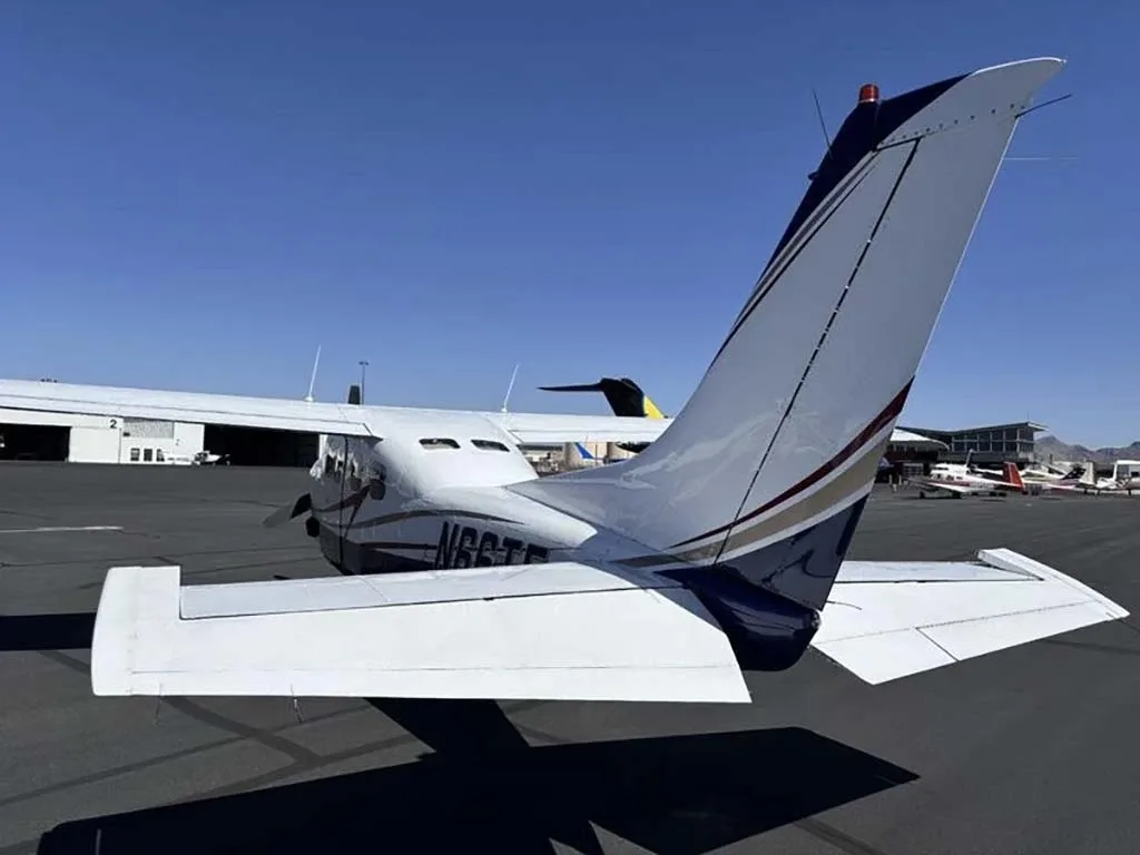 A rear-quarter view of the white and blue Cessna 210 Centurion with registration N66TE on an airfield.