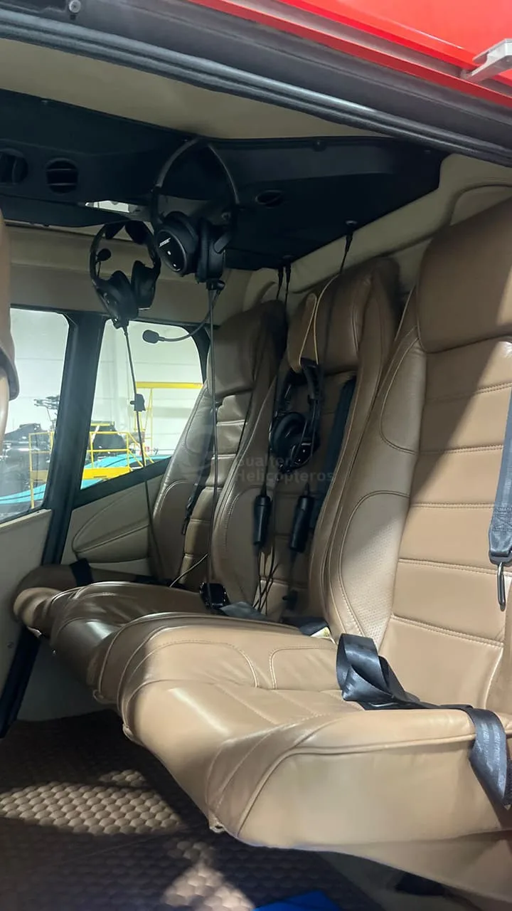 The interior of a helicopter shows three rows of brown leather passenger seats with headsets hanging above.
