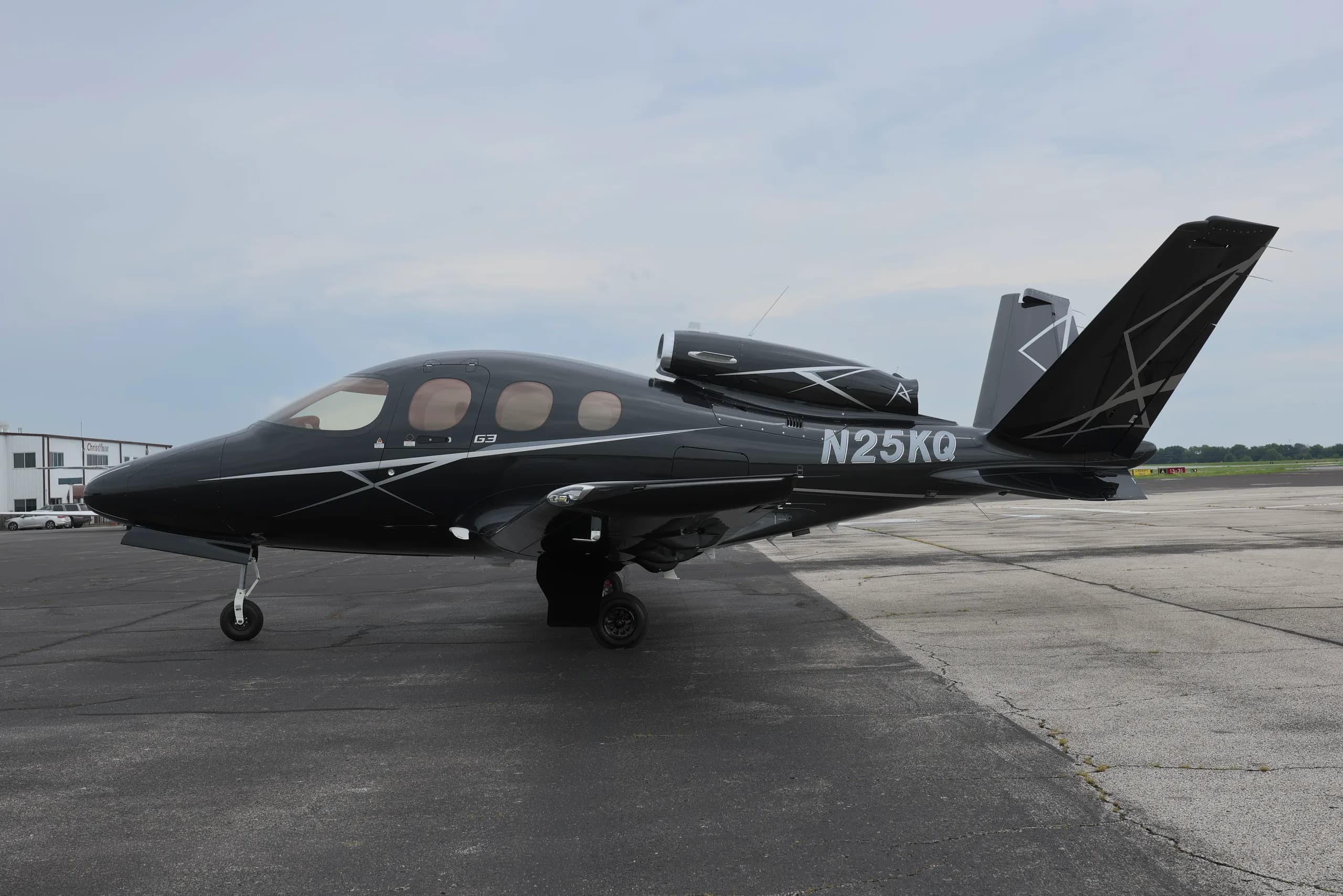 A black Cirrus Vision Jet SF50, N25KQ, with white accents is parked on an airport tarmac.
