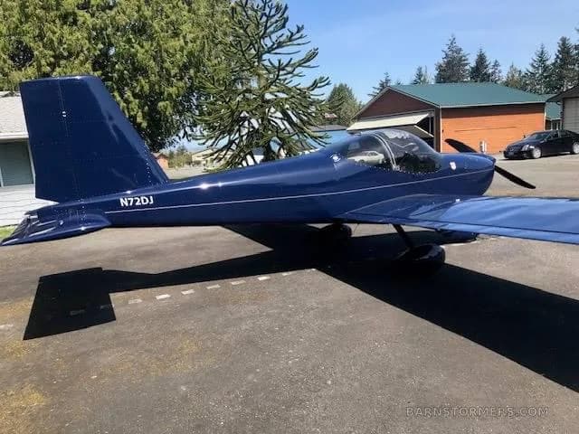 A dark blue single-engine aircraft with tail number N72DJ is parked on a concrete pad, showing its right side and propeller.