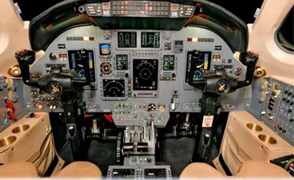 The detailed cockpit of a private jet, showing the instrument panel with multiple displays, yokes, and control levers.